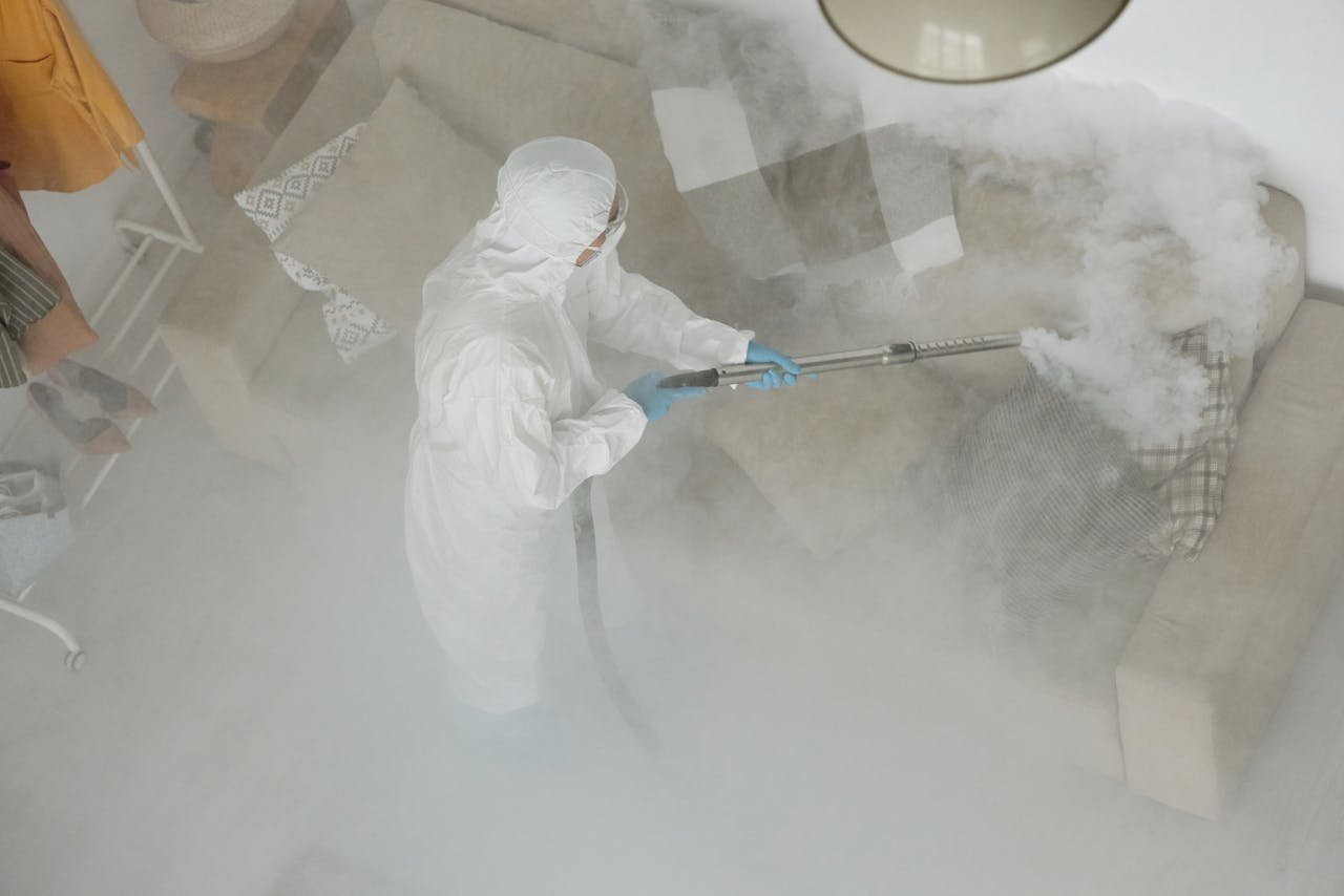 Technician in protective gear sanitizing a living room with smoke fumigation.